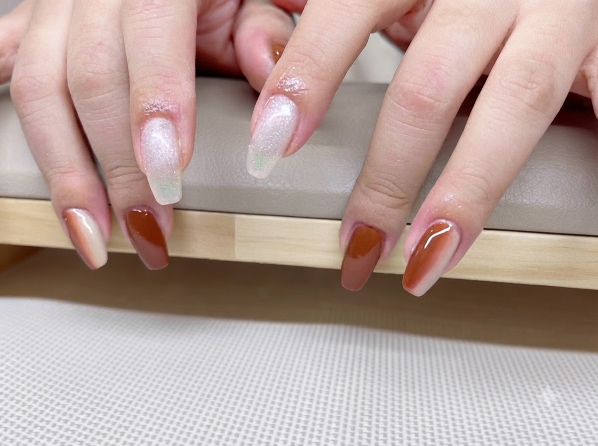 A close-up view of hands showing a caramel and amber gradient manicure with glowing cat-eye shimmer lines.