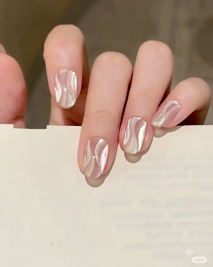 A fine liner brush drawing a delicate, curved ribbon shape with silver cat eye gel on top of the nude base.