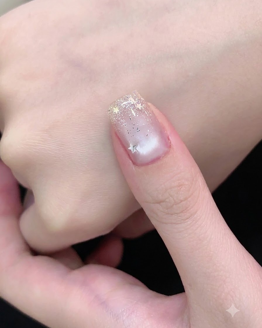 A nail brush applying a clear top coat over a nail decorated with silver glitter and star pieces.