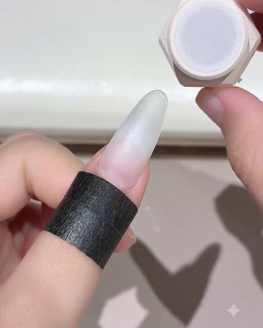 A finger with a prepped nail held near a nail gel jar, ready for curing.
