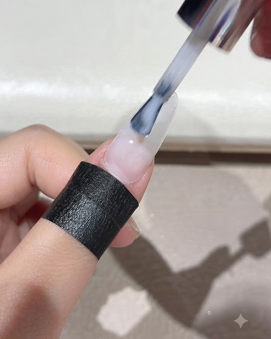 A brush spreading milky white self-leveling gel evenly over the entire surface of the nail.
