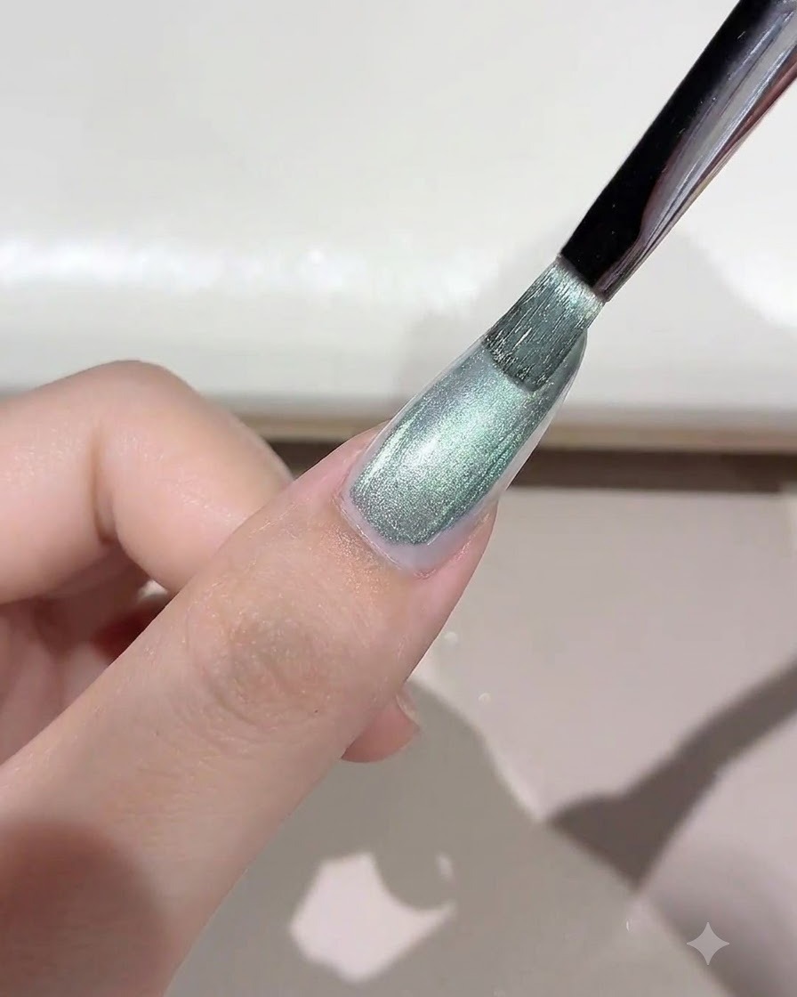 A brush applying a shimmering green-toned wild cat-eye gel onto the nail.