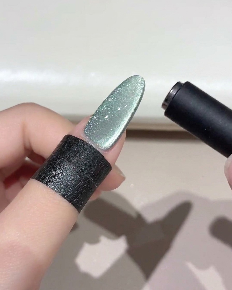 A black magnetic tool hovering over a shimmering green cat-eye nail to shape the light band.