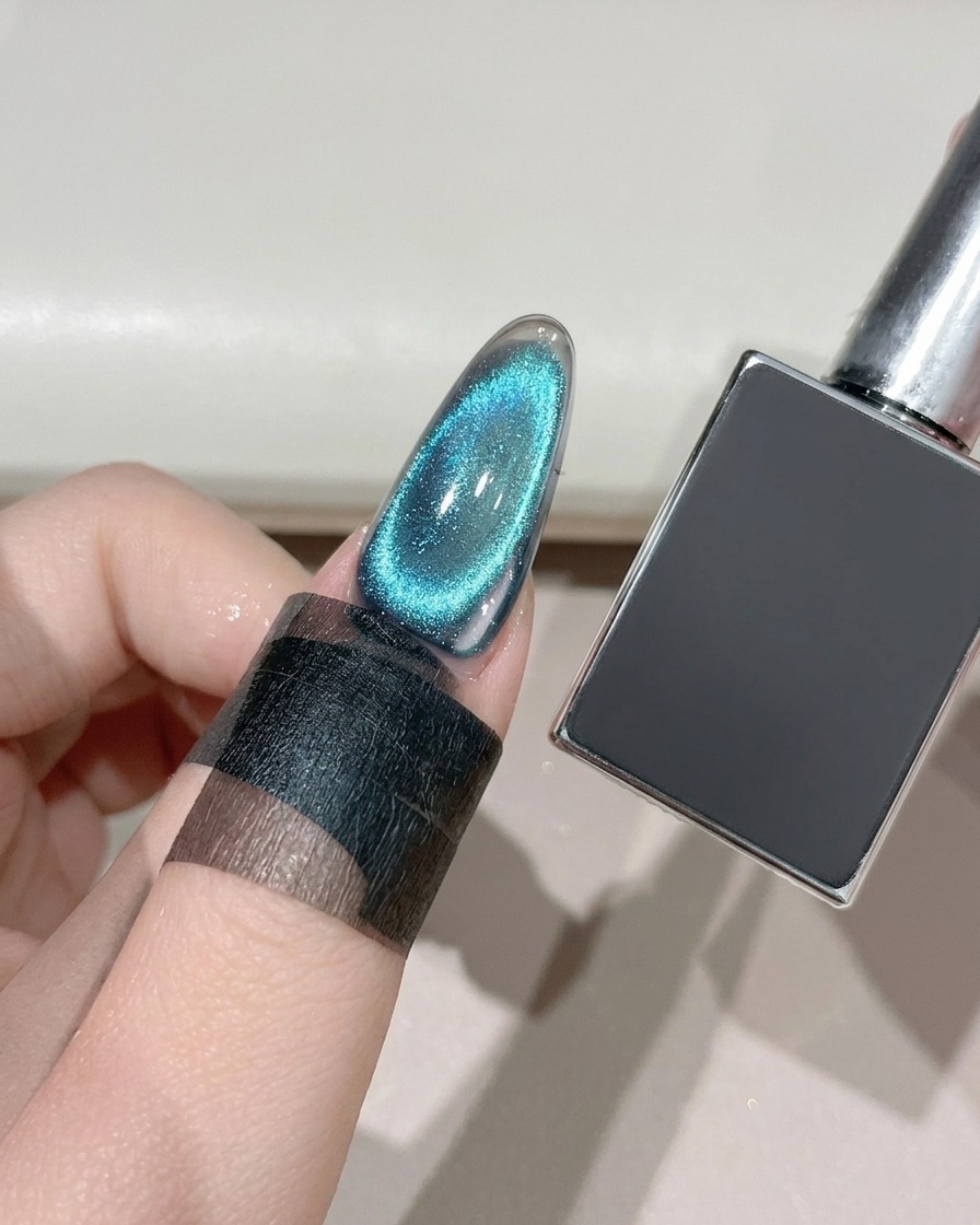 A finished cat-eye nail being cured under a UV/LED lamp next to a dark gel bottle.