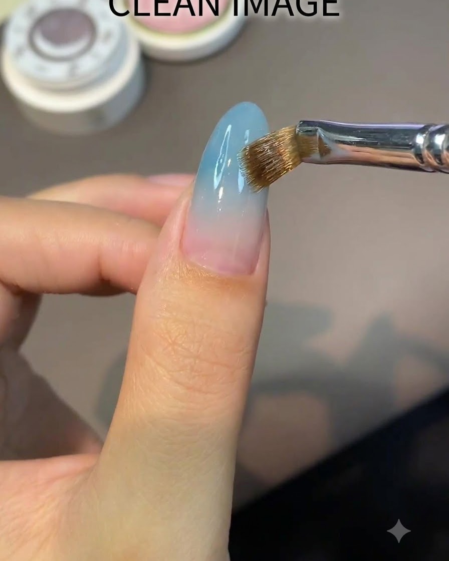 A flat brush applying a clear nude base gel evenly onto an almond-shaped nail.