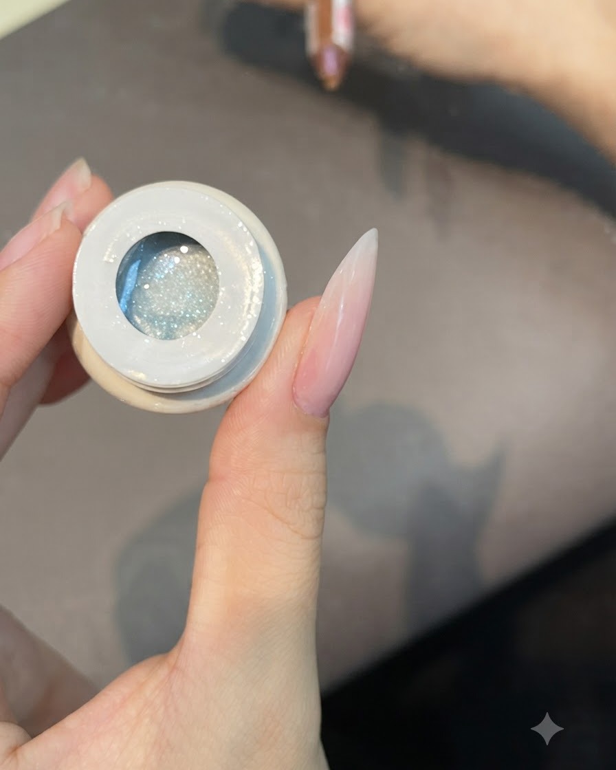 A flat brush dipping into an open pot of translucent cat eye gel polish number 49.