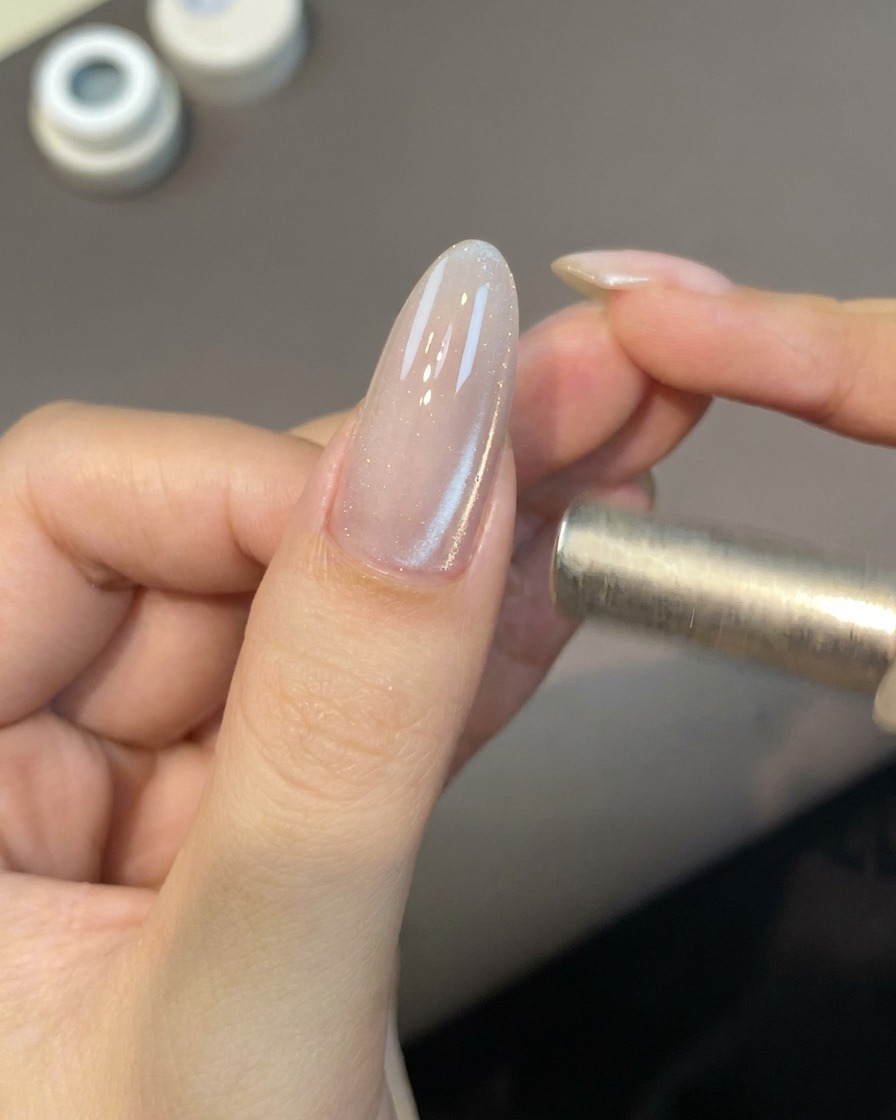 A small magnetic wand tool hovering near a nail to activate the cat eye gel particles.