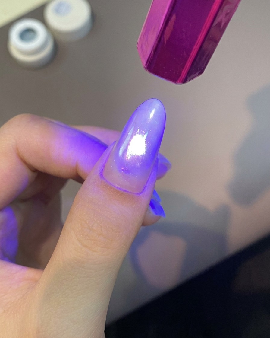 A handheld purple UV nail lamp shining bright light over a manicured finger to cure the gel coating.