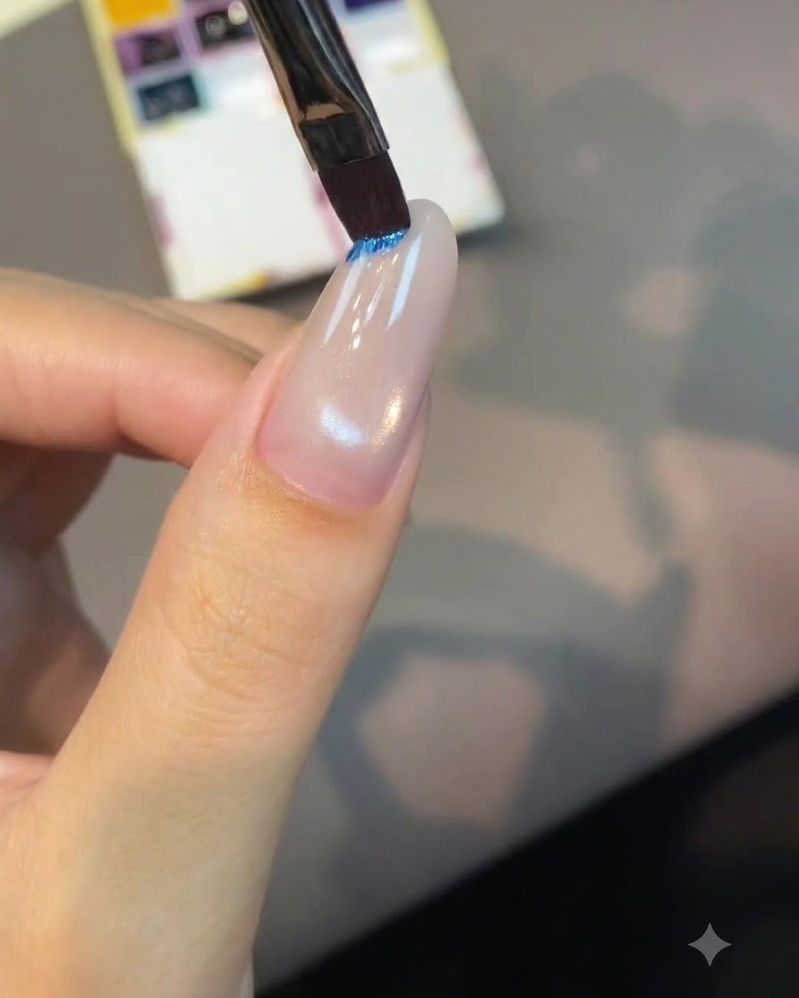 A flat nail art brush dipping into a bright blue pigment pan on a palette.