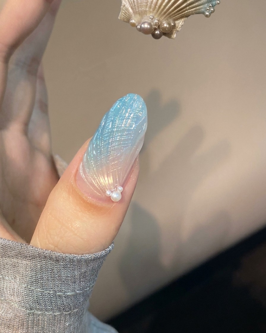 A fingernail with blue and translucent shell nail art placed under a purple UV lamp curing.