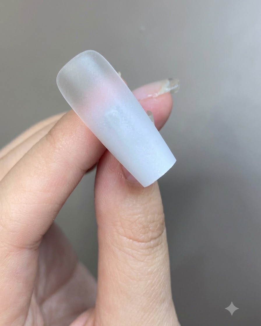 A thin layer of translucent milky white gel being brushed over the gradient nail surface.