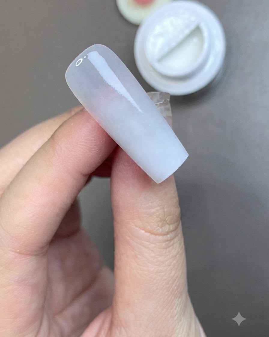 A brush applying a smooth coat of matte top coat over a milky white prepped nail.