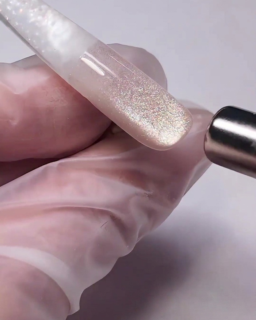 A cylindrical magnetic wand held close to wet cat-eye gel on a nail, pulling the metallic particles to create a shimmer.