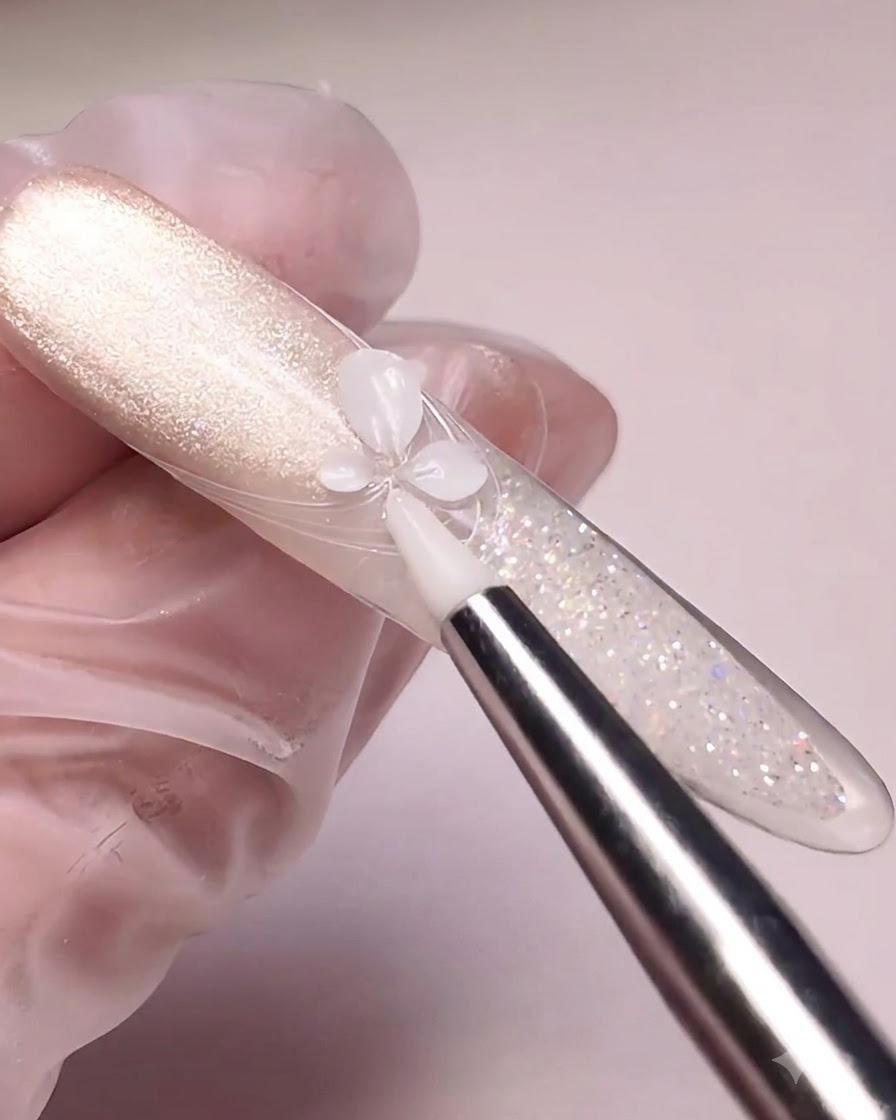 A silicone tool pressing white carving gel into flower petals on a cat-eye painted nail tip.