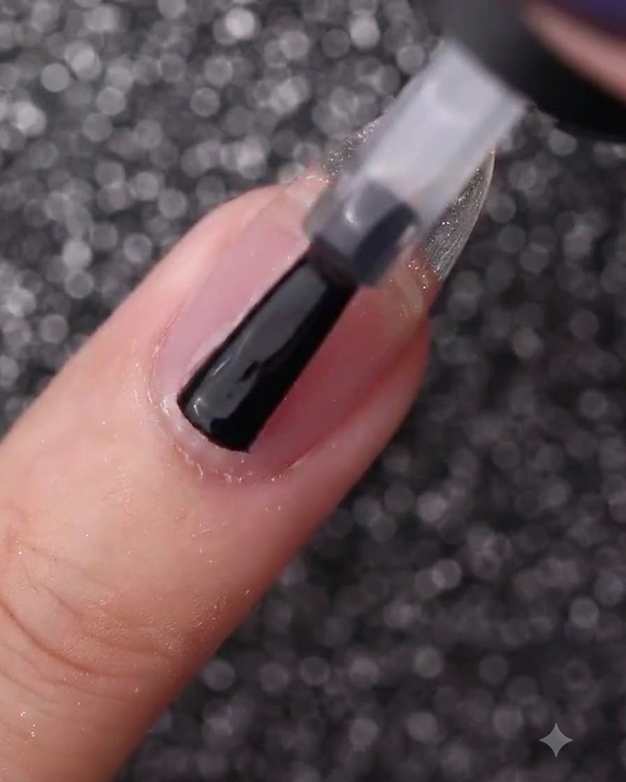 A hand using a bottle brush to coat a bare natural nail with clear base gel.