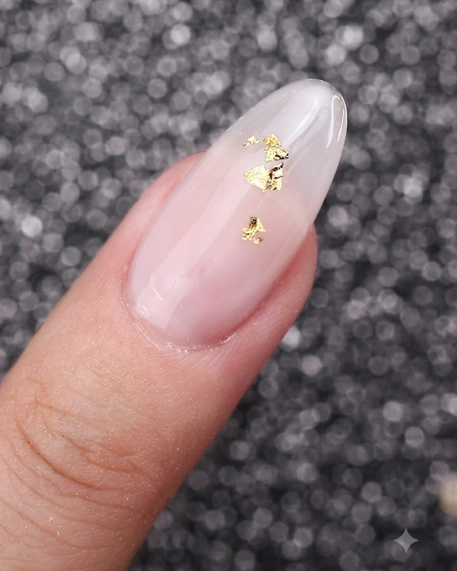 A close-up view of gold foil flakes delicately placed on top of a milky white gel manicured nail.