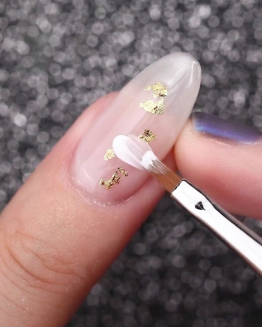 An angled petal brush creating white flower petals on a milky white nail with gold foil accents.