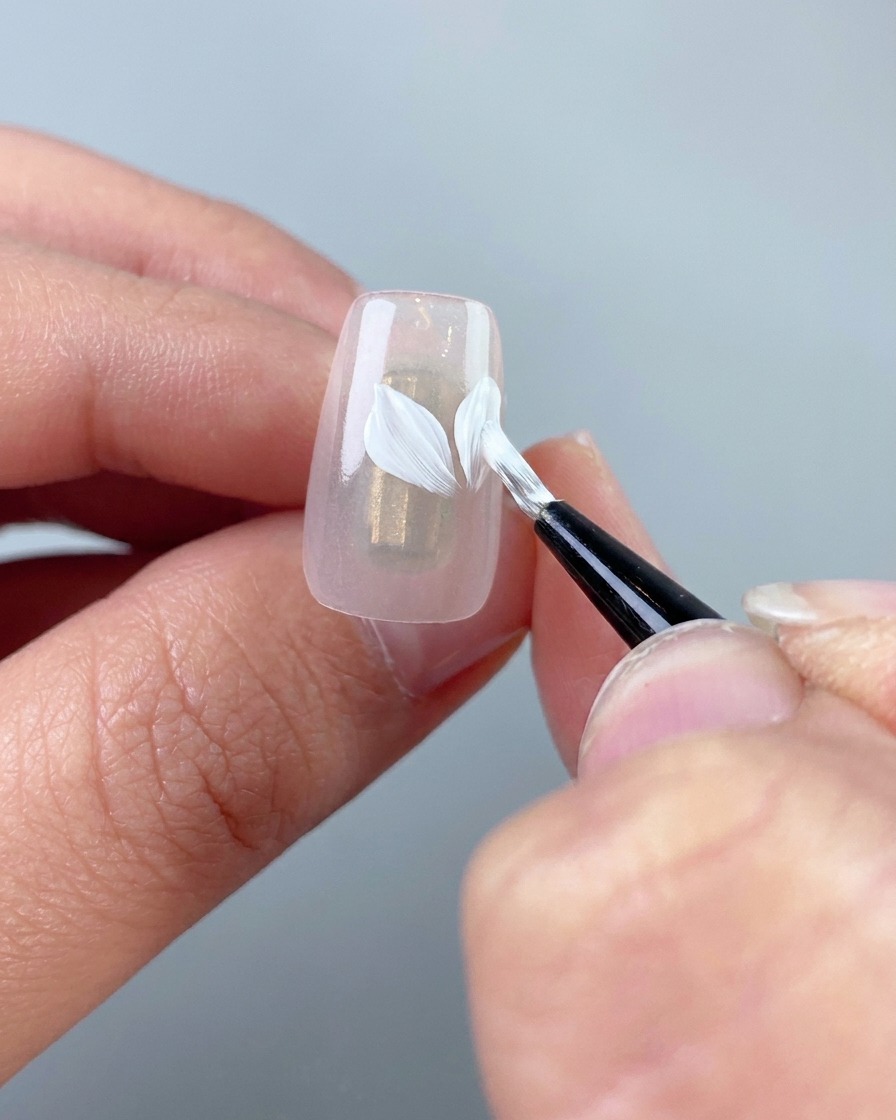 A close-up showing smaller white petals being painted onto the nail.