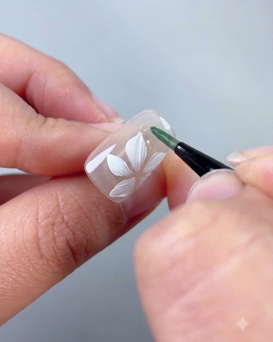 A liner brush applying green gel to form a thin leaf next to the white flower.