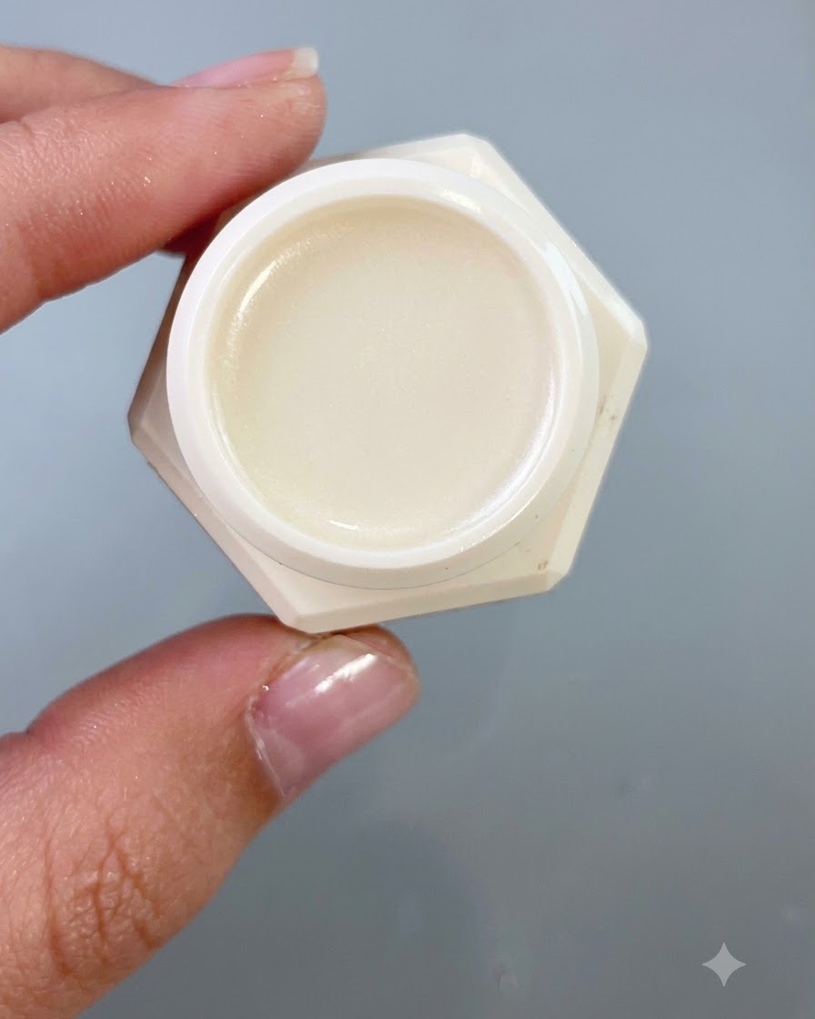 A close-up of a small jar containing transfer patting gel, held against a neutral gray background.