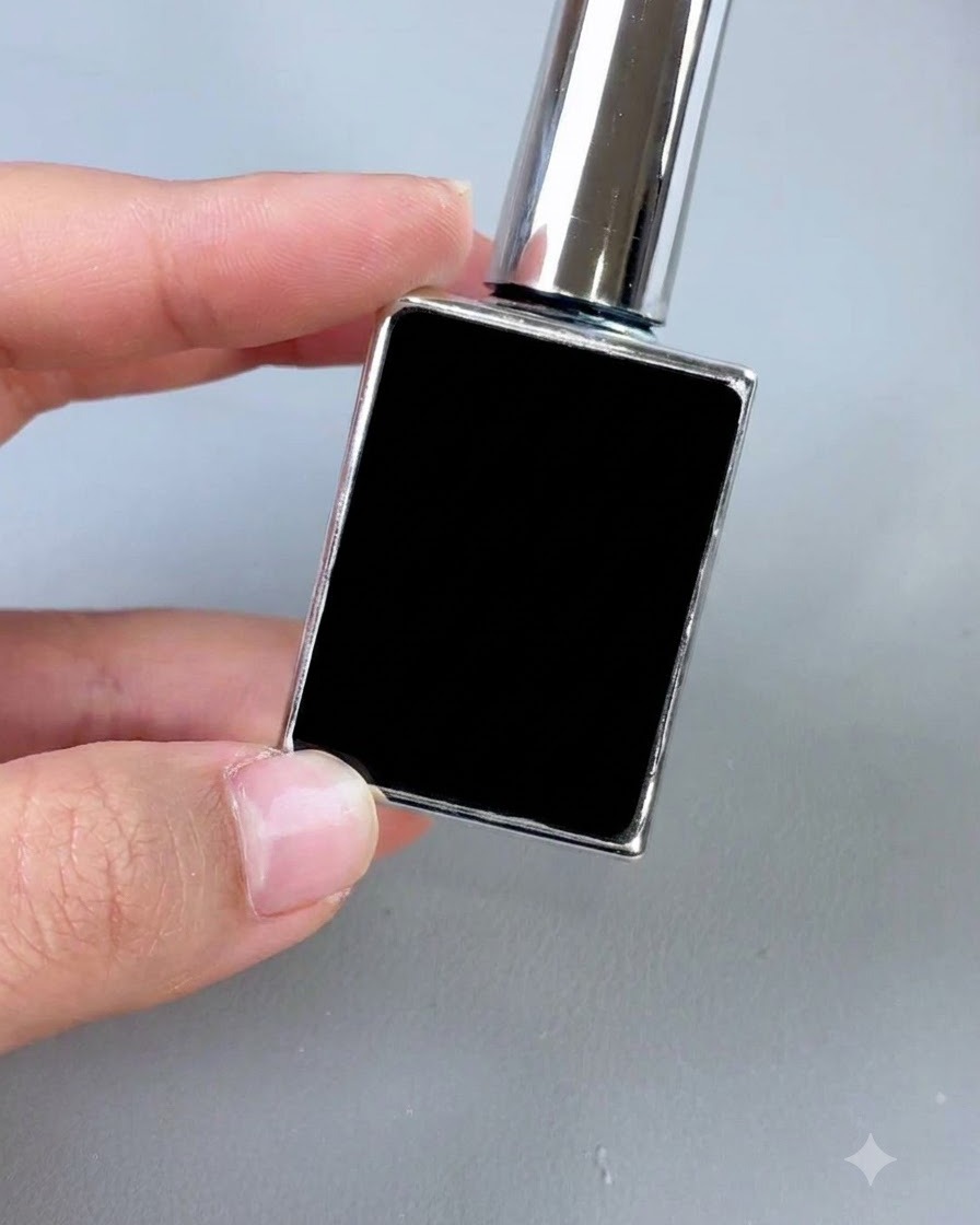 A small black cosmetic bottle with a silver cap and applicator brush, displayed upright against a gray background.
