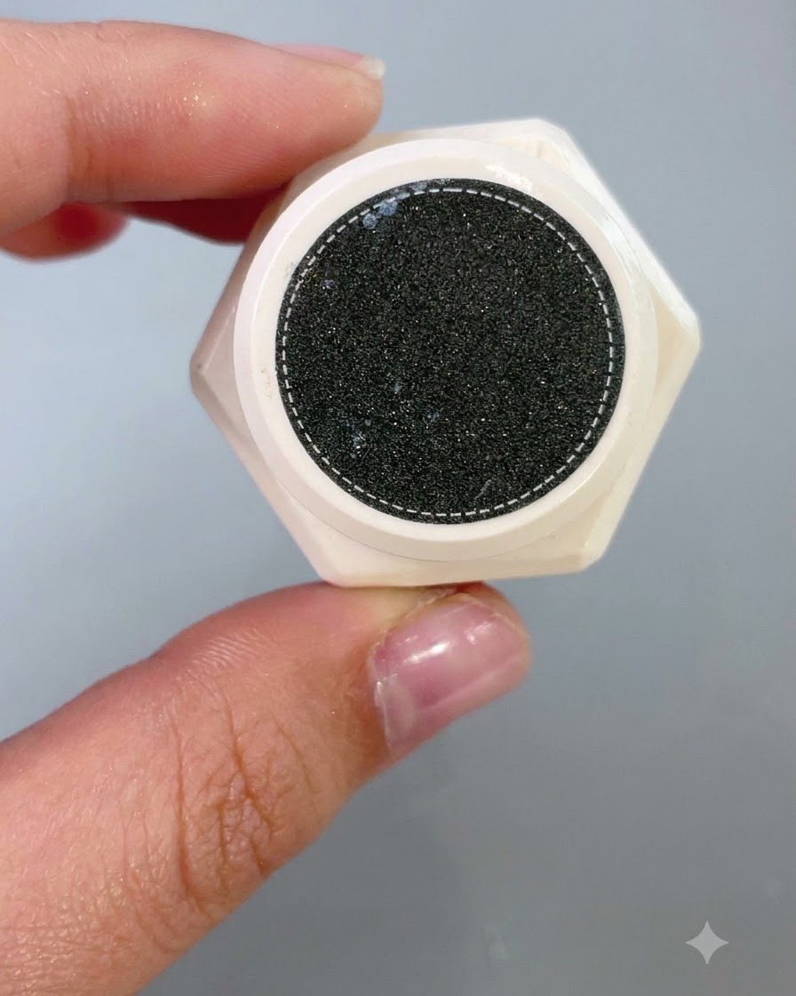 A close-up view looking down into the open jar of a textured sculpting product with a speckled dark surface.