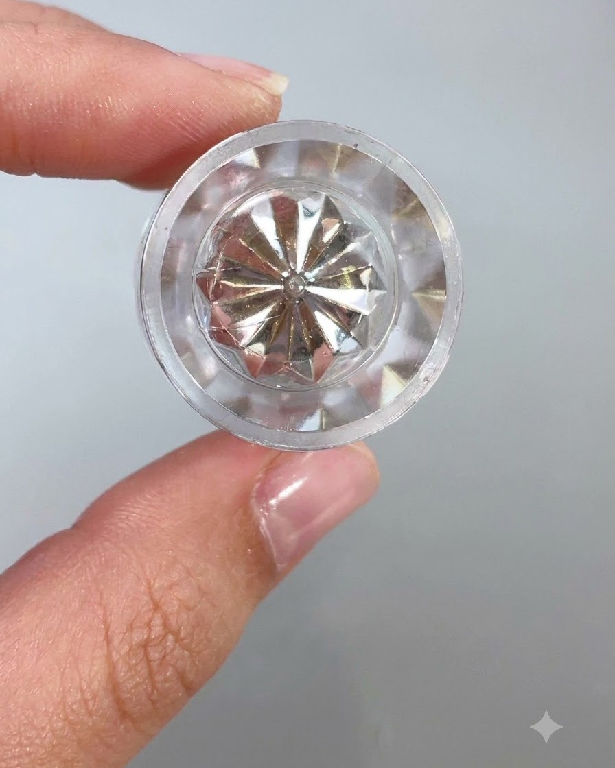 A close-up view of a clear, faceted crystal container top or applicator tool reflecting light against a light background.