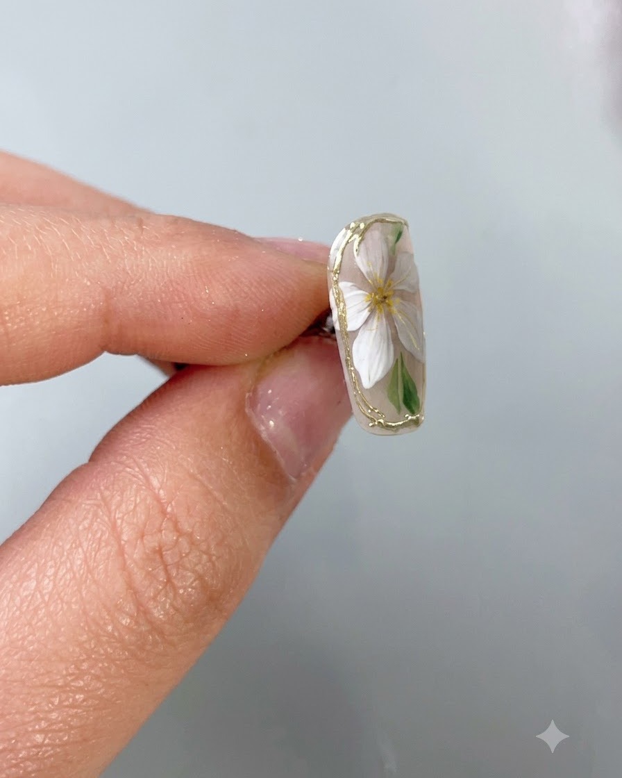 A fine nail art brush applying a clear protective top coat precisely over a delicate gold chrome border on a nude base nail.