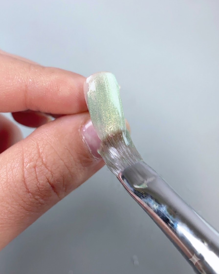 A nail brush smoothing a sheer green cat-eye gel layer over a press-on nail surface.