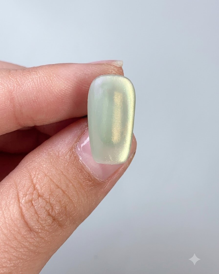 A nail brush applying top coat over a green cat eye gel nail.