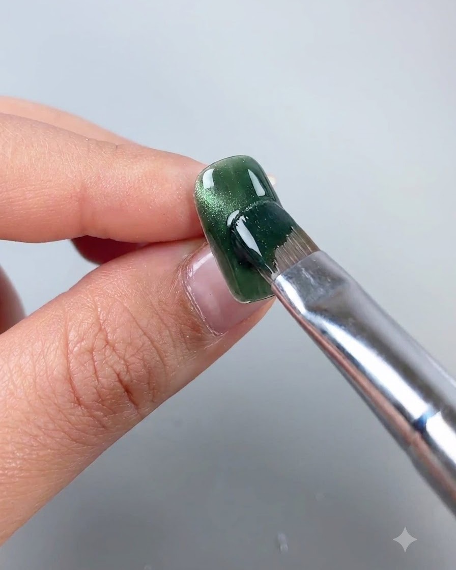 A magnetic wand being held near a green cat eye gel nail to shift the magnetic particles into a side arc line.