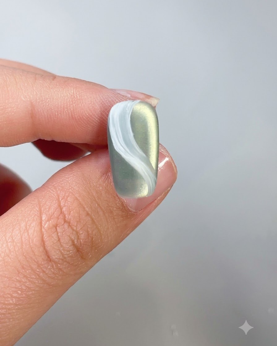A close-up of a nail with a white cloud design being coated with top coat.