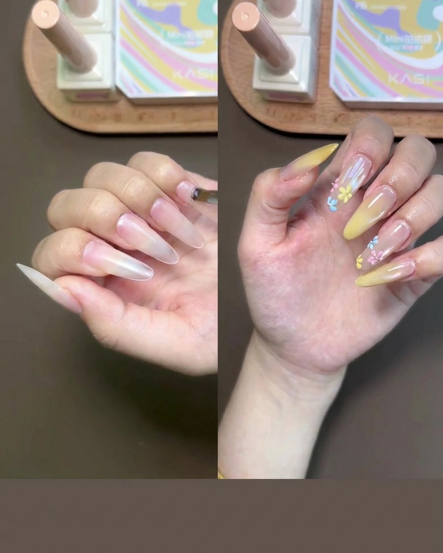 A close-up of a hand having nude base gel applied to the fingernails with a small brush.