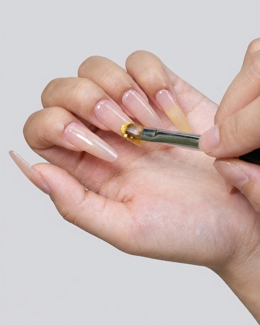 A close-up of a brush applying yellow gel polish to the nail tip.