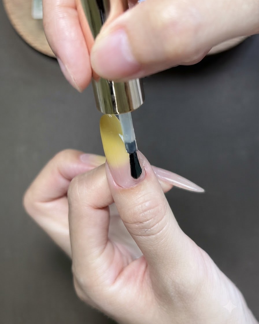 A brush applying cat-eye gel polish over the yellow gradient thumb nail.