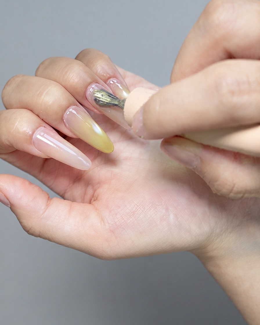 A strong magnet tool hovering over a glossy cat-eye gel nail to shape the magnetic particles.