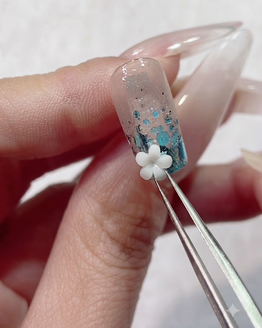 Precision tweezers placing a white 3D acrylic flower charm onto the wet gel near the nail cuticle.