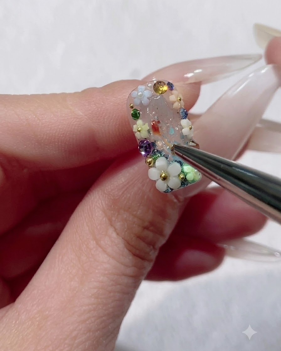A fine liner brush applying hard top coat around the base edges of a 3D floral charm on a nail.