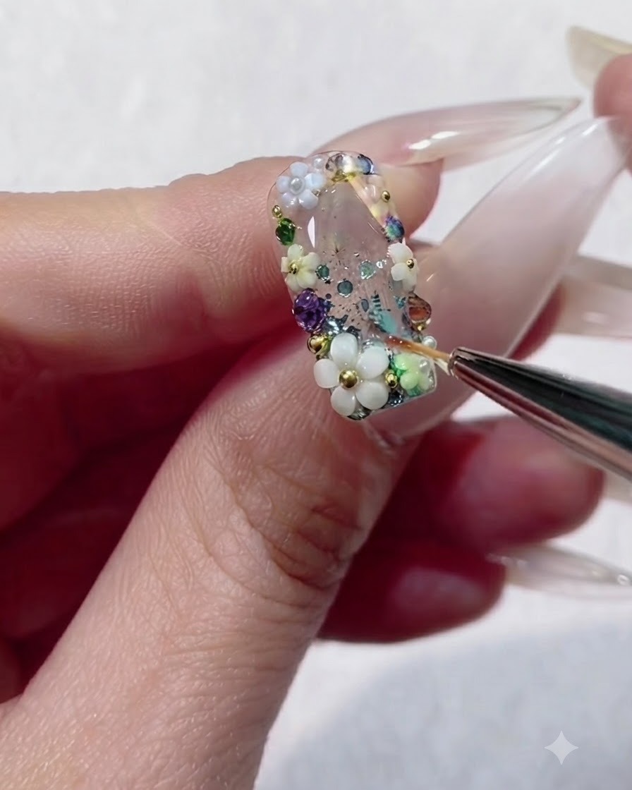 A liner brush flooding the tiny spaces between colorful rhinestones and beads on a clear gel nail.