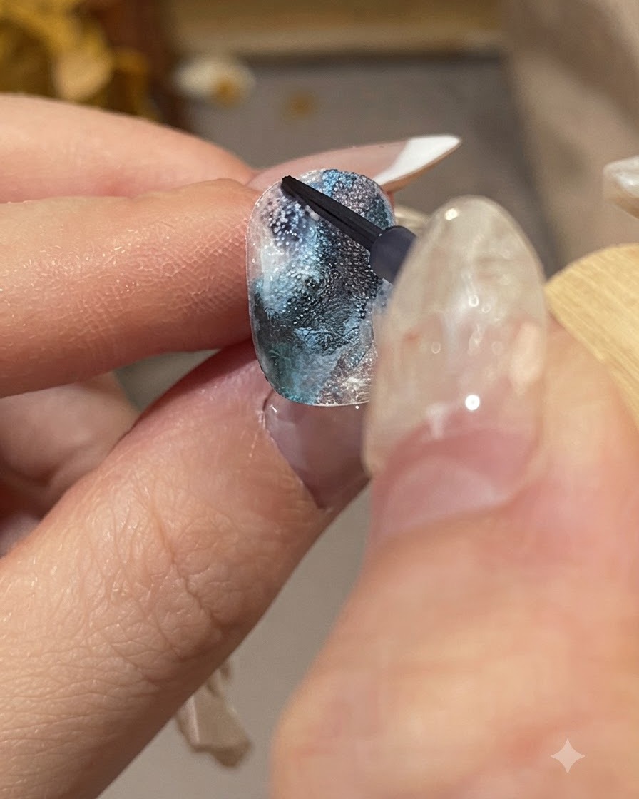 A detailed close-up of a manicured hand holding a fine brush to apply dark blue ink droplets onto a textured nail surface.