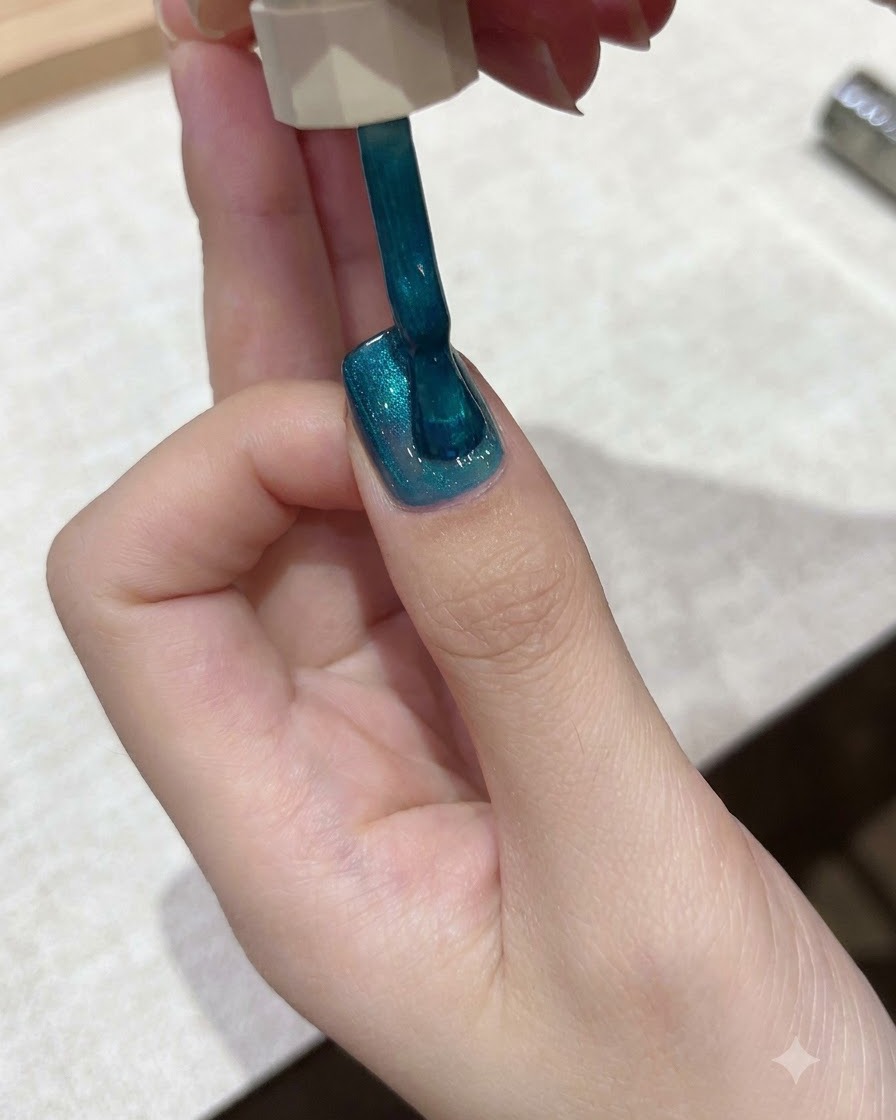 A brush applying vibrant teal-blue cat-eye gel polish over a nail surface.