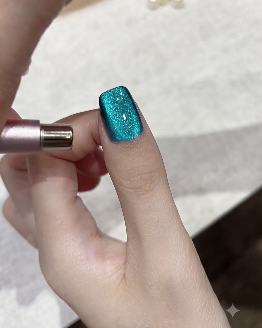 A magnetic tool adjusting the light reflection on a teal blue cat-eye gel nail.