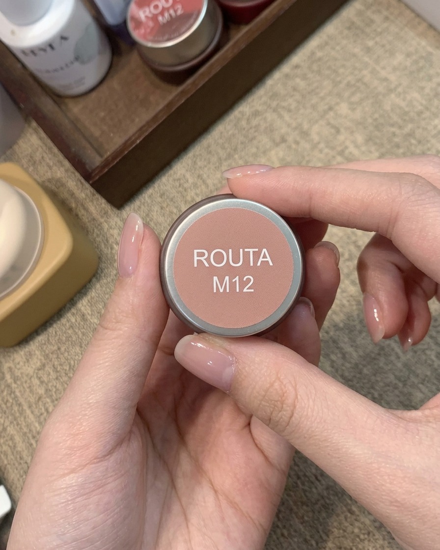 A small jar labeled Routa M12 holding a warm peachy-pink blush gel color.
