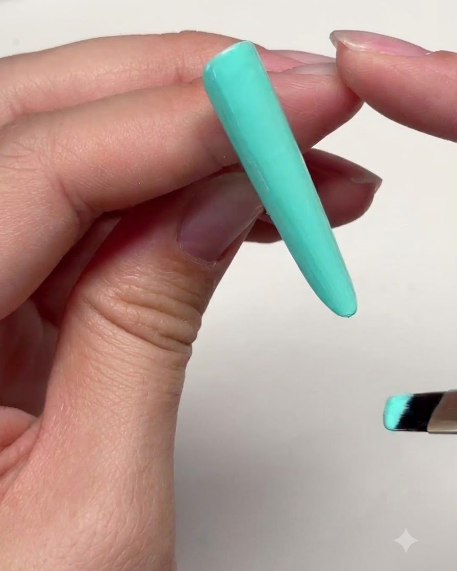 A long mint green nail extension with a thin layer of gel applied near the top cuticle boundary.