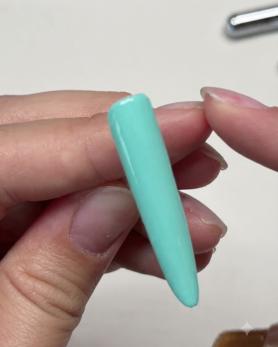A brush applying a matte top coat over the solid mint green nail extension.