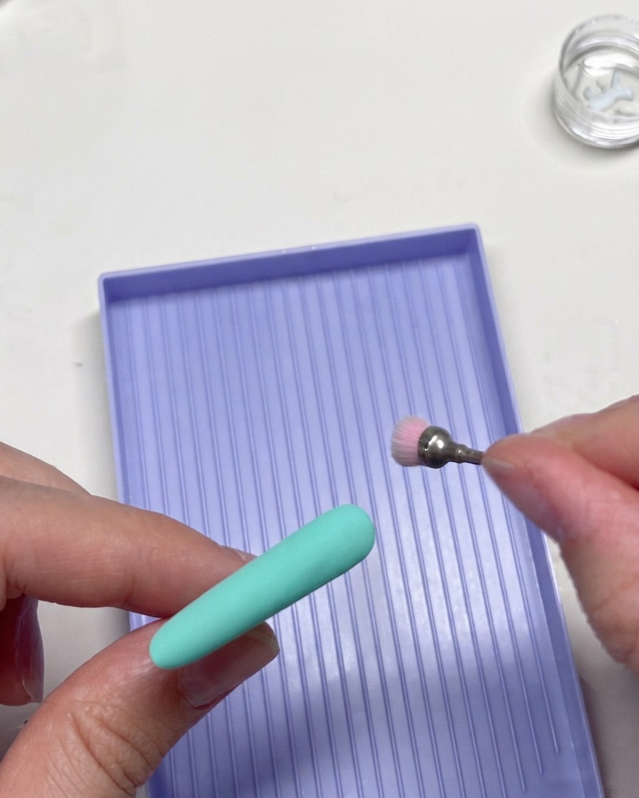 A rotary milling drill bit tool gently refining the edges of a mint green nail tip.