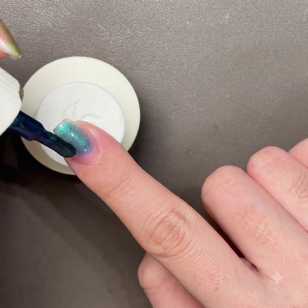 A black magnetic wand hovering over a dark blue-green painted nail to manipulate the cat-eye polish.