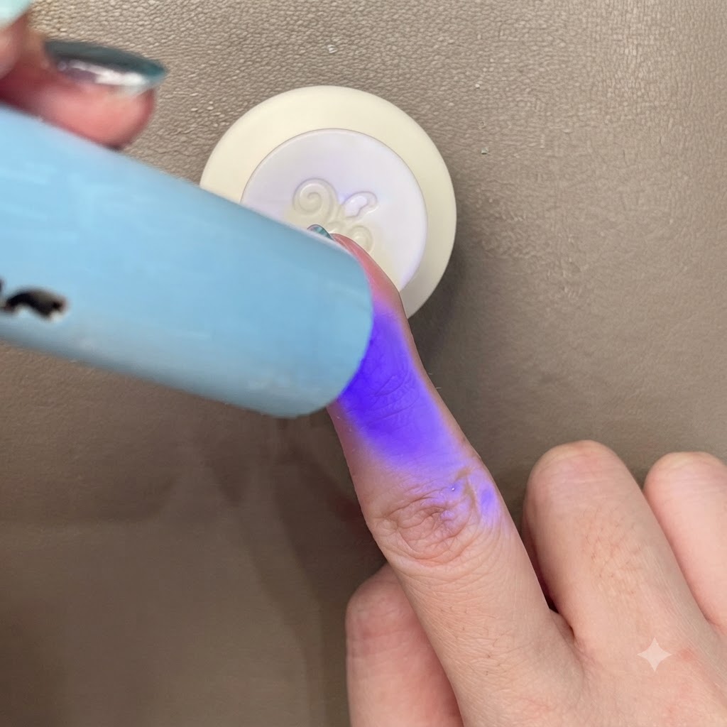 Curing a blue-green cat-eye nail under a small portable blue UV/LED light.