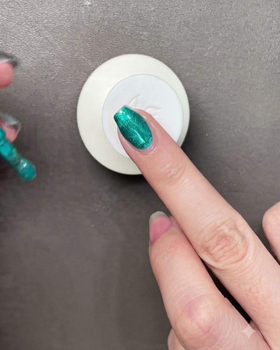 A brush applying vibrant metallic green gel polish onto a fingernail with a small magnet visible nearby.