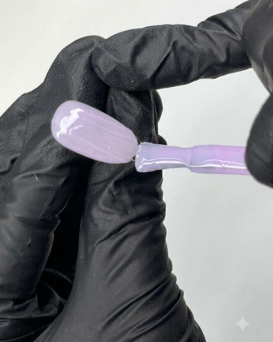 A flat brush gliding N04 sheer purple gel polish evenly across the surface of an oval practice nail tip.